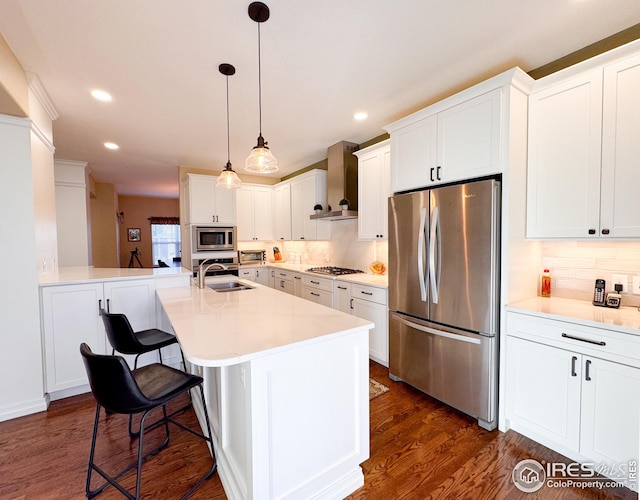 kitchen featuring a kitchen bar, a sink, dark wood finished floors, stainless steel appliances, and wall chimney range hood