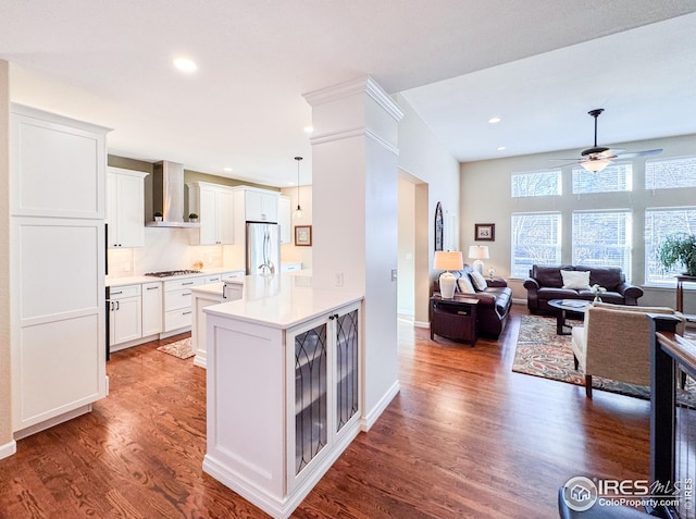 kitchen with open floor plan, wood finished floors, gas stovetop, freestanding refrigerator, and wall chimney range hood