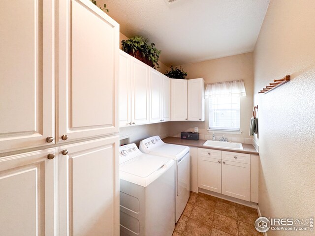 clothes washing area with washer and dryer, cabinet space, a textured wall, and a sink