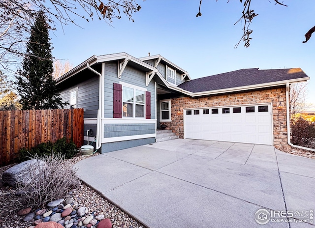 view of front of house with stone siding, concrete driveway, a garage, and fence