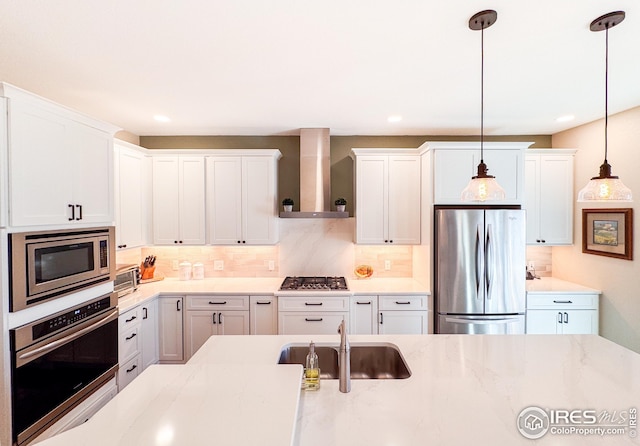 kitchen featuring a sink, hanging light fixtures, appliances with stainless steel finishes, wall chimney exhaust hood, and backsplash