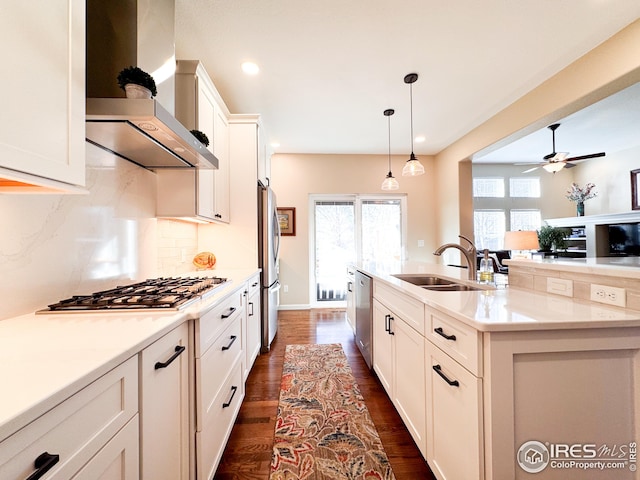 kitchen with tasteful backsplash, wall chimney range hood, appliances with stainless steel finishes, white cabinets, and a sink