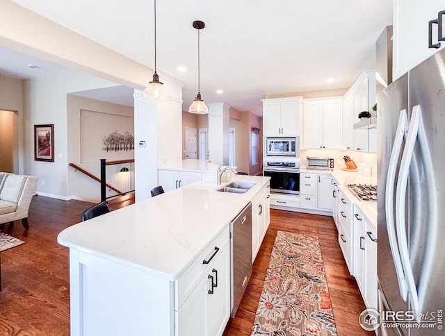 kitchen with an island with sink, a sink, backsplash, dark wood finished floors, and stainless steel appliances