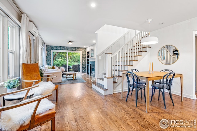 dining area with baseboards, an AC wall unit, wood finished floors, and stairs