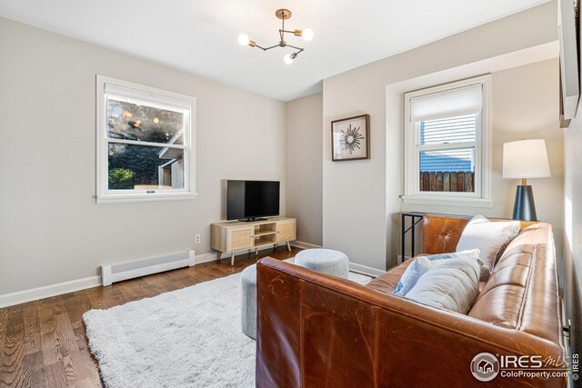living room featuring an inviting chandelier, wood finished floors, baseboards, and a baseboard radiator