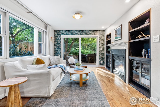 living area featuring a glass covered fireplace, built in features, wood finished floors, and recessed lighting