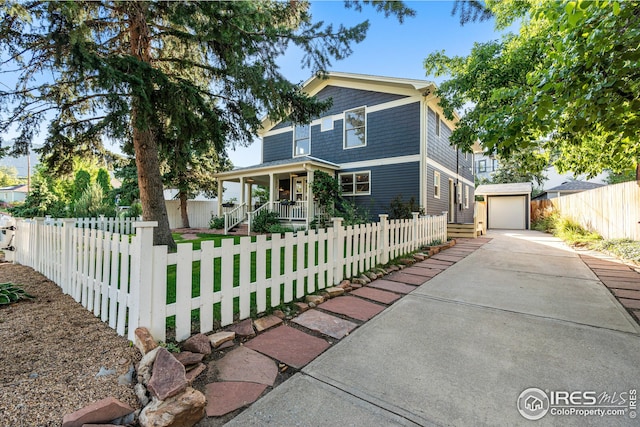 view of front of property featuring a fenced front yard, a detached garage, a porch, an outdoor structure, and concrete driveway