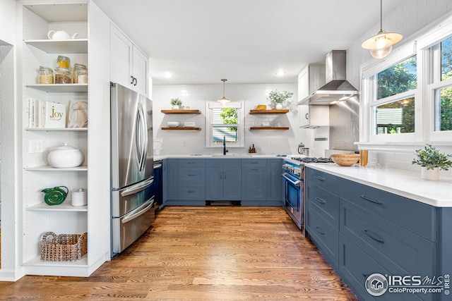 kitchen with open shelves, blue cabinetry, appliances with stainless steel finishes, and wall chimney exhaust hood
