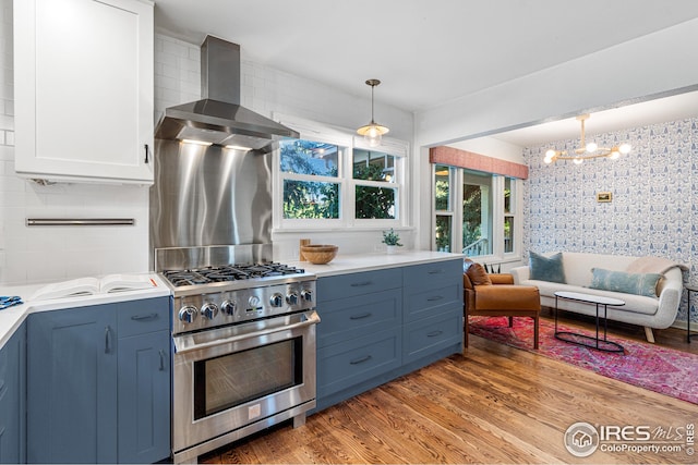 kitchen featuring wood finished floors, hanging light fixtures, high end stainless steel range oven, wall chimney range hood, and a chandelier