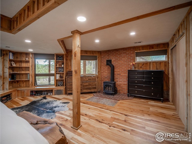 bedroom featuring wooden walls, multiple windows, a wood stove, and wood finished floors