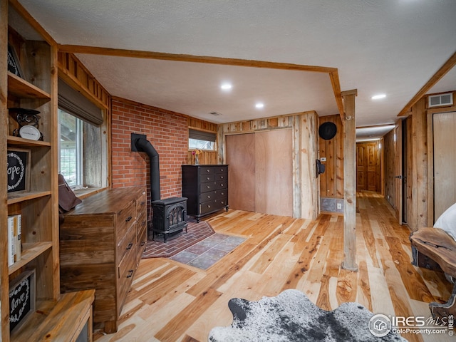 living area featuring visible vents, plenty of natural light, hardwood / wood-style floors, wooden walls, and a wood stove