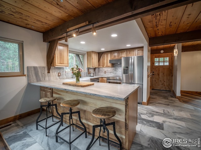 kitchen featuring under cabinet range hood, beam ceiling, stainless steel fridge, and tasteful backsplash