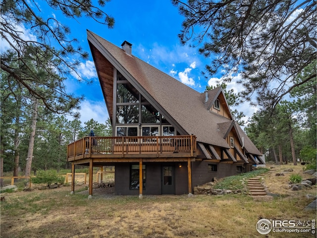 rear view of house featuring a deck, a yard, and roof with shingles