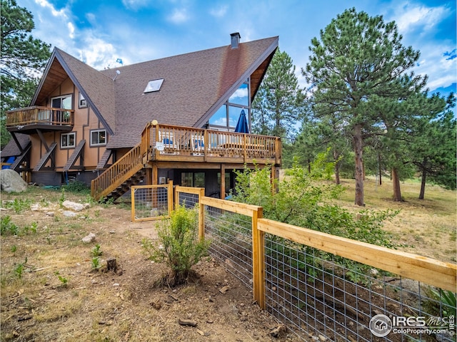 rear view of property with roof with shingles, a deck, stairs, and fence