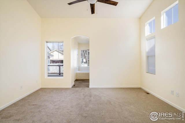 unfurnished room featuring baseboards, arched walkways, carpet floors, and ceiling fan