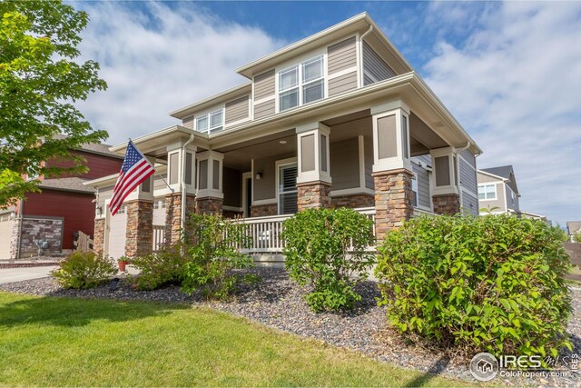 prairie-style home featuring driveway, stone siding, a porch, fence, and an attached garage