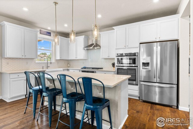 kitchen featuring white cabinets, appliances with stainless steel finishes, wall chimney range hood, and a sink