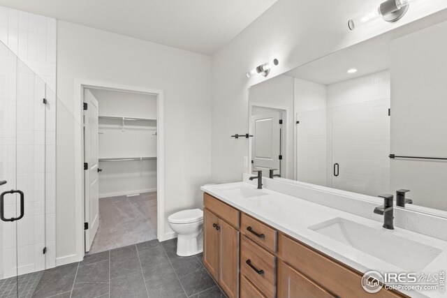 full bathroom featuring double vanity, a stall shower, a walk in closet, and a sink