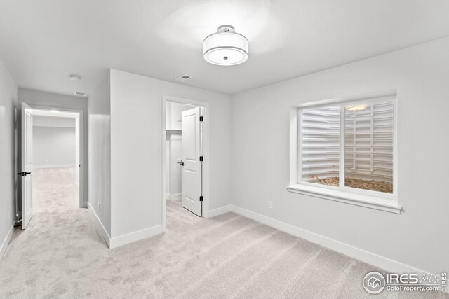 unfurnished bedroom featuring a walk in closet, visible vents, light colored carpet, and baseboards