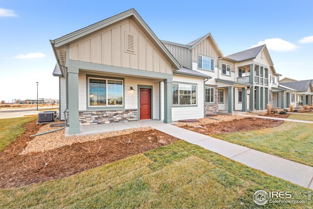 view of front of property featuring board and batten siding, a porch, a front yard, central AC unit, and stone siding