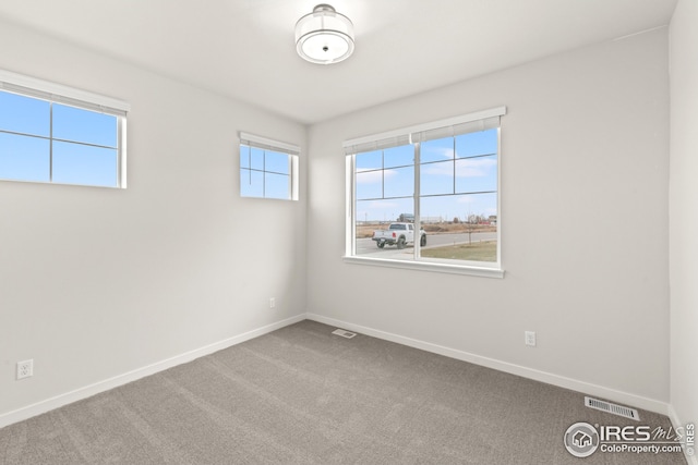empty room with carpet, visible vents, and baseboards