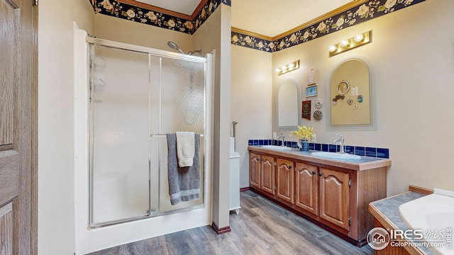 bathroom featuring wood finished floors, a sink, double vanity, and a stall shower