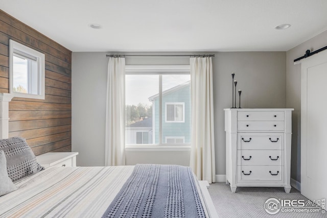 unfurnished bedroom featuring carpet flooring, wood walls, baseboards, and a barn door