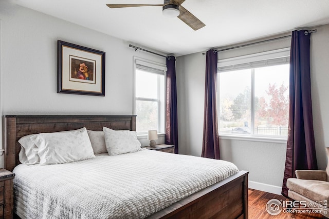 bedroom featuring a ceiling fan, multiple windows, dark wood-style floors, and baseboards