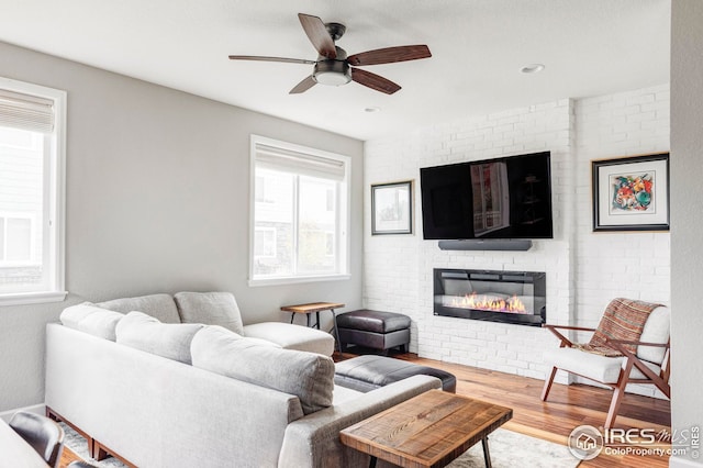 living area with a brick fireplace, wood finished floors, and ceiling fan