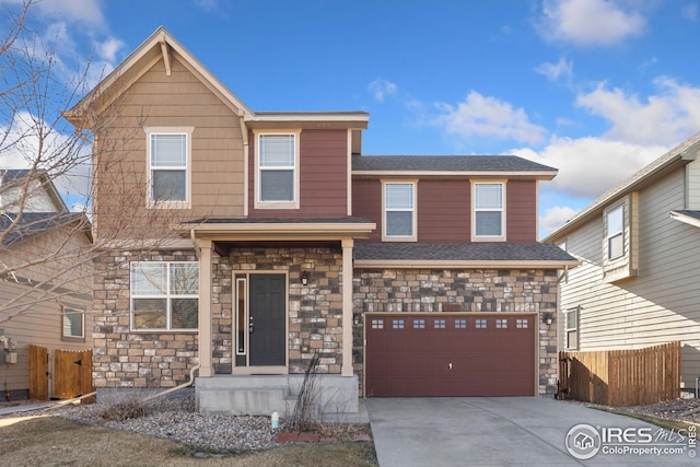 traditional-style home featuring a garage, driveway, stone siding, and fence