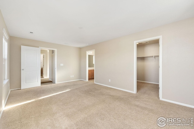 unfurnished bedroom with baseboards, a walk in closet, and light carpet