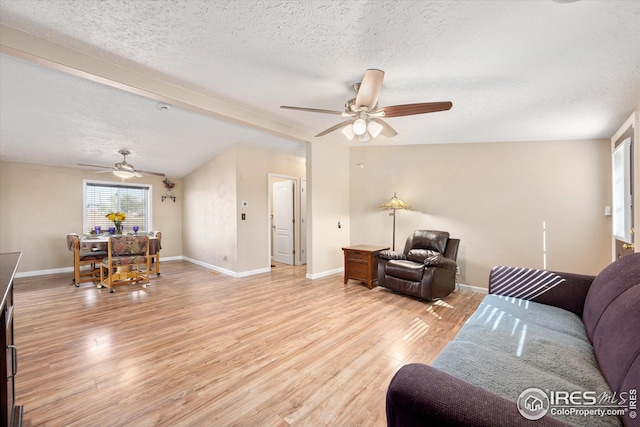 living area featuring baseboards, ceiling fan, vaulted ceiling, light wood-style flooring, and a textured ceiling