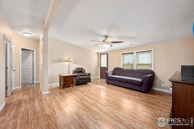 living area with baseboards, light wood-style flooring, a textured ceiling, and ceiling fan