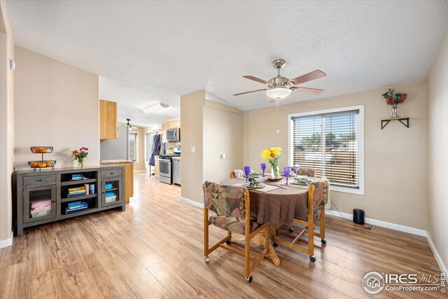 dining area featuring light wood-style flooring, a ceiling fan, baseboards, and a textured ceiling