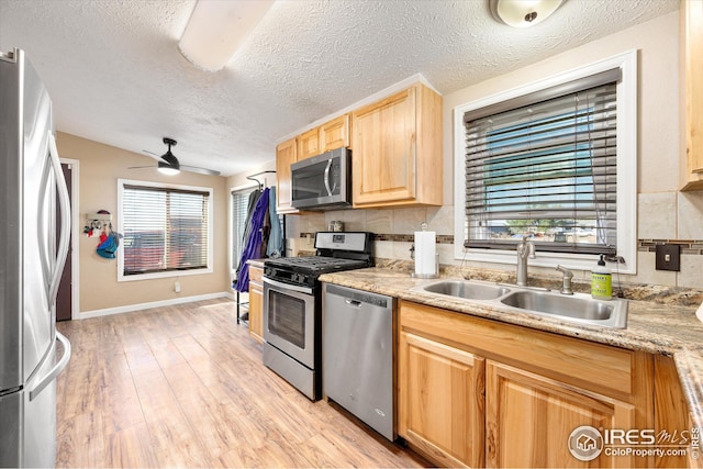 kitchen featuring light wood finished floors, light brown cabinetry, light countertops, appliances with stainless steel finishes, and a sink