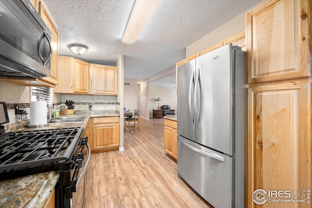 kitchen with light brown cabinets, gas range, light countertops, freestanding refrigerator, and a sink
