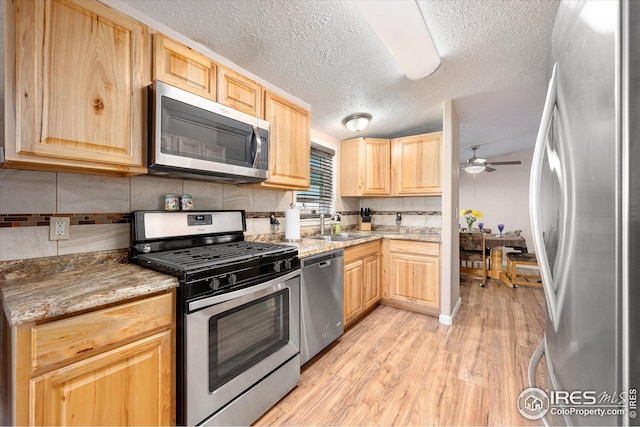 kitchen featuring light wood-style flooring, a ceiling fan, light brown cabinets, a sink, and appliances with stainless steel finishes