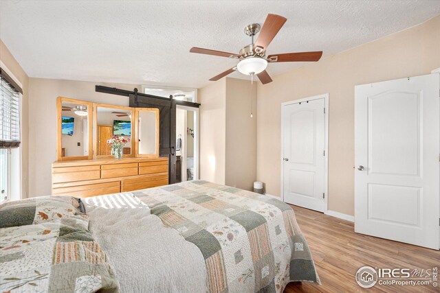 bedroom featuring baseboards, light wood-type flooring, a barn door, a textured ceiling, and a ceiling fan