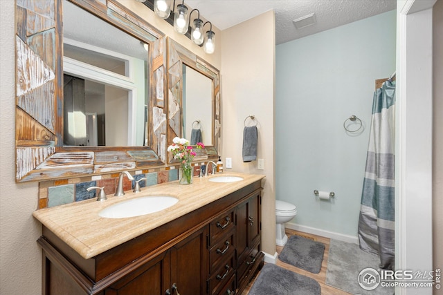 full bath with a textured ceiling, double vanity, toilet, and a sink