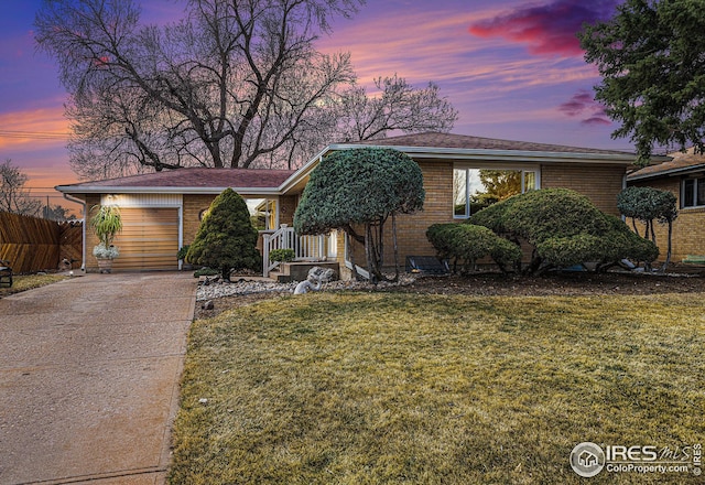 view of front of house featuring a lawn, driveway, fence, and brick siding