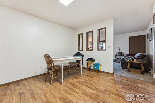 dining space featuring baseboards, light wood-type flooring, and a textured ceiling