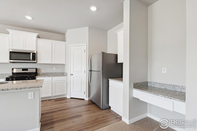 952 Cascade Falls St, Severance, CO 80550 - kitchen with appliances with stainless steel finishes, white cabinets, light stone counters, recessed lighting, and wood finished floors
