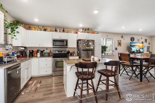 4216 Yellowbells Dr, Evans, CO 80620 - kitchen featuring appliances with stainless steel finishes, white cabinetry, a center island, wood finished floors, and recessed lighting