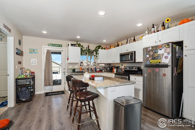 4216 Yellowbells Dr, Evans, CO 80620 - kitchen featuring stainless steel appliances, dark wood-type flooring, white cabinetry, a kitchen bar, and a kitchen island