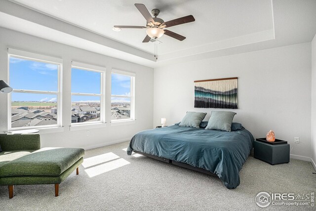 carpeted bedroom with ceiling fan, baseboards, and a tray ceiling