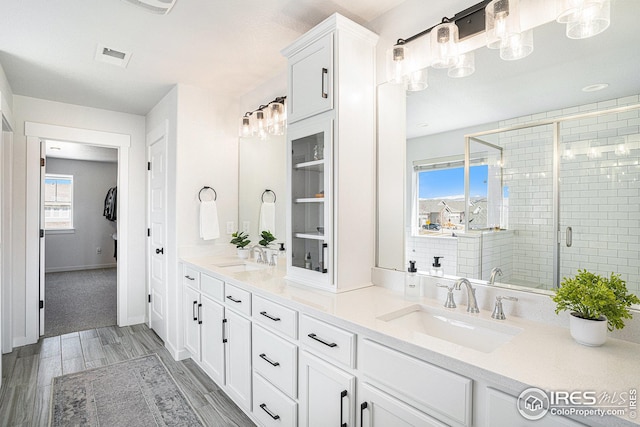 full bath featuring a shower stall, wood finish floors, double vanity, and a sink