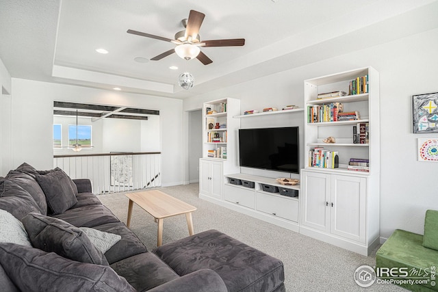 carpeted living area with built in features, recessed lighting, a tray ceiling, and a ceiling fan