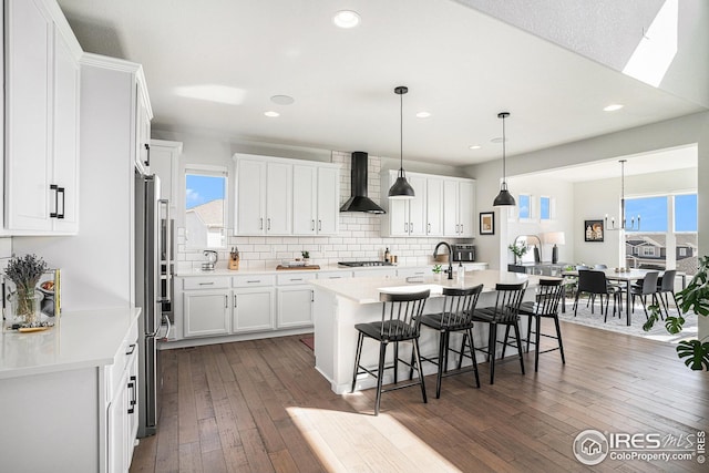 kitchen with a kitchen bar, white cabinets, wall chimney exhaust hood, and wood-type flooring