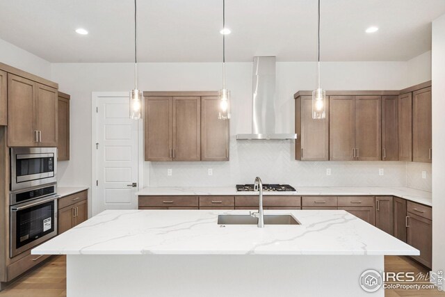 kitchen featuring light stone counters, a sink, tasteful backsplash, stainless steel appliances, and wall chimney range hood