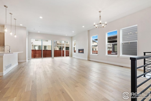 unfurnished living room with visible vents, a chandelier, light wood finished floors, recessed lighting, and a sink